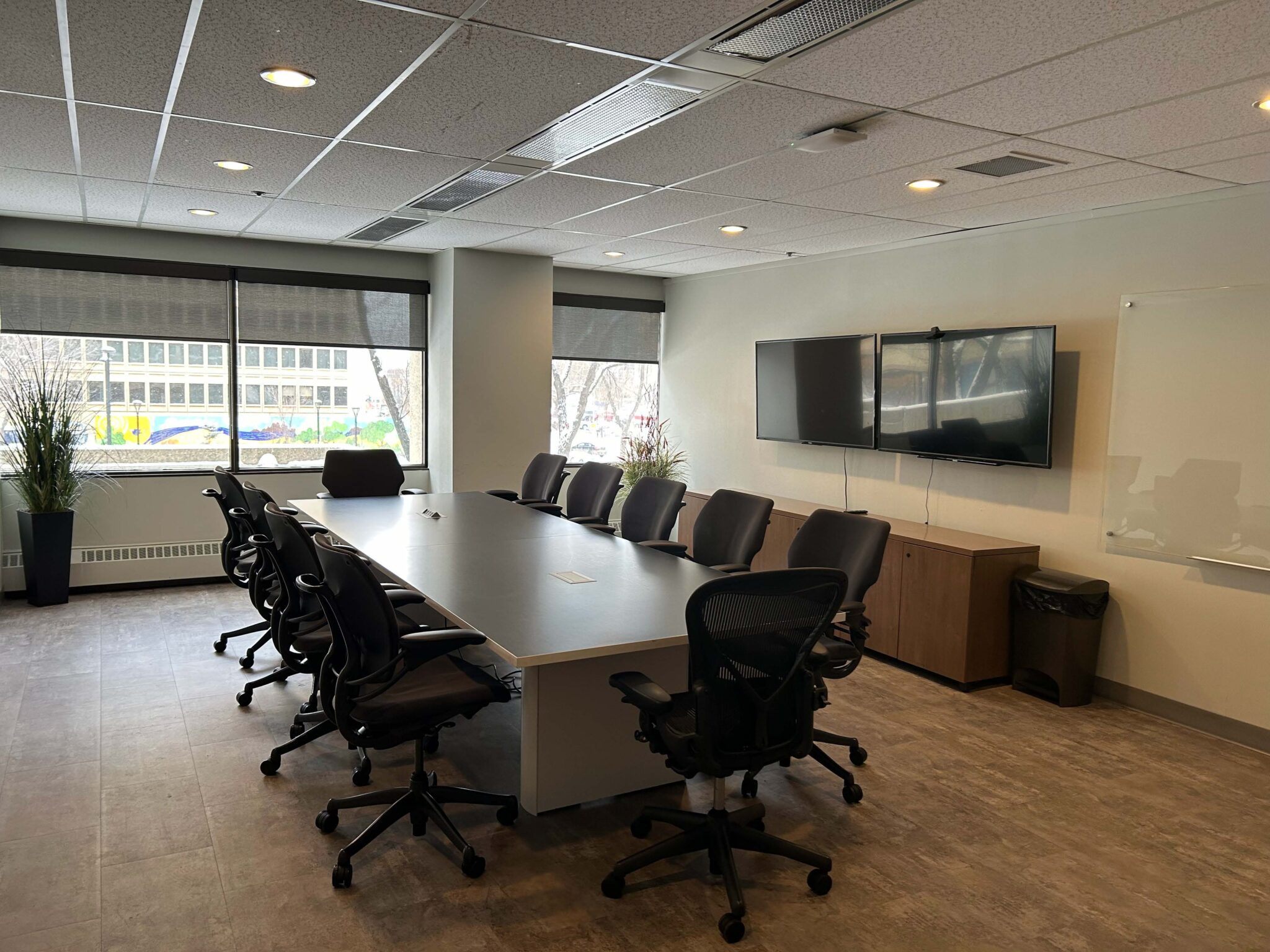 Meeting room with a board room table, chairs, windows and large screens on the wall