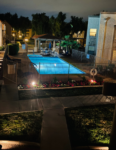 Apartment pool at night surrounded by apartments and palm trees.